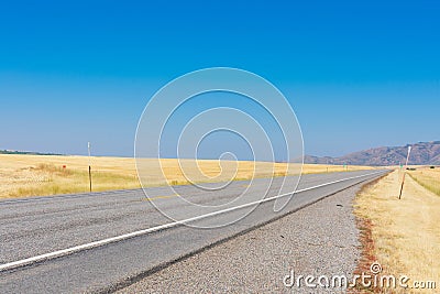 Empty two way road navigates between scenic agriculture fields toward hills under blue sky Stock Photo