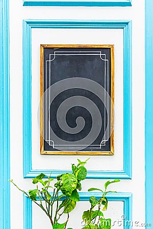 Empty vertical blackboard framed in brown, white and light blue wood. A natural plant with green leaves at the bottom. Copy space Stock Photo