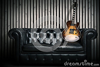 Empty vintage sofa and electric guitar with modern wood wall recording studio background. Music concept with nobody Stock Photo