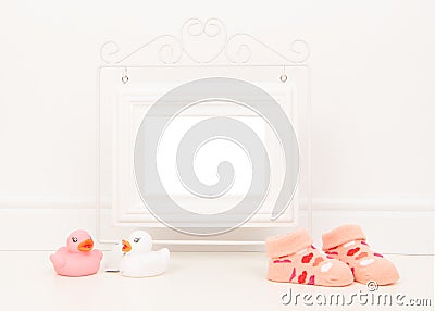 Empty white picture frame with space for text or wishes in a white living room setting with pink baby sock and pink and white rubb Stock Photo