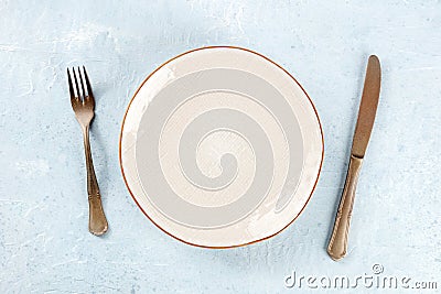 An empty white plate with a gold rim, with a fork and a knife, overhead Stock Photo