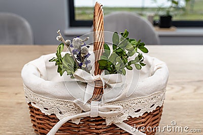 An empty wicker Easter basket, decorated with boxwood and catkins, standing on a table. Stock Photo