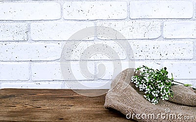 Empty wooden table with flowers and burlap fabric on white bricks wall background. Stock Photo