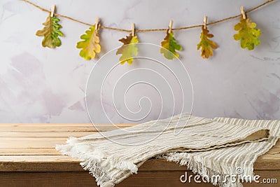 Empty wooden table with modern tablecloth over autumn leaves garland background. Autumn kitchen mock up for design and product Stock Photo