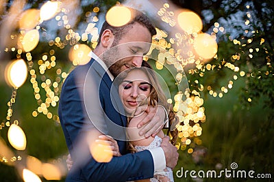 Enamored newlyweds gently embrace. Wedding ceremony in nature. The lights of the electric garland illuminate the wedding Stock Photo