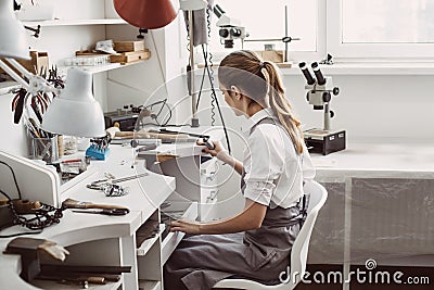 The End of the Working Day. Side view of young female jeweler sitting at her jewelry workshop and cleaning her workplace Stock Photo
