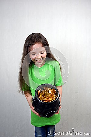 Endearing laughting girl in green T-shirts showing off cast iron pot with four-petal lucky shamrock leaf Stock Photo