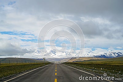 Endless straight road to snow mountains on plain with blue sky and white clouds Stock Photo