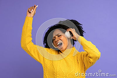 Energized biracial woman sing along, wears wireless headphones, has good mood, isolated on violet background. Happy dark skinned Stock Photo