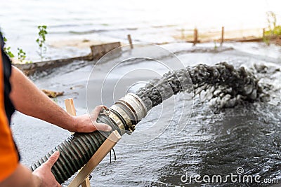 Engeneer hold pipe of power pump machine pouring mud sludge waste water with sand silt on ground. Sand-wash and coast-depeening. Stock Photo