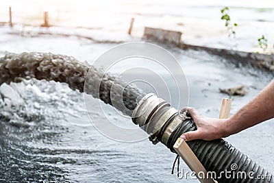 Engeneer hold pipe of power pump machine pouring mud sludge waste water with sand silt on ground. Sand-wash and coast-depeening. Stock Photo