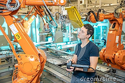 Engineer controls using remote control of industrial robot in factory. Automatic welding and gluing using automation and Stock Photo