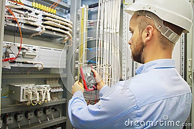 Engineer electric with multimeter. Side view of male technician examining fusebox with multimeter probe. Stock Photo