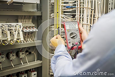 Engineer electrician with multimeter in hands at electric automation box panel. Service engineer tests circuit of industrial Stock Photo