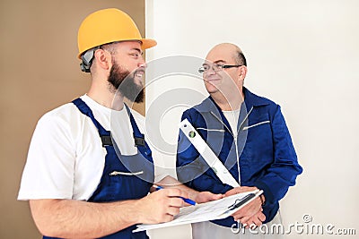 Engineer with his colleague, construction worker is measuring wall using spirit level tool, checking in apartment blueprint. Stock Photo