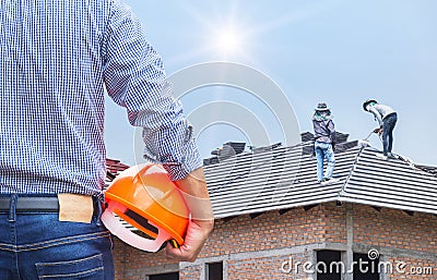 Engineer holding yellow safety helmet at new home building with workers installing concrete tile Stock Photo