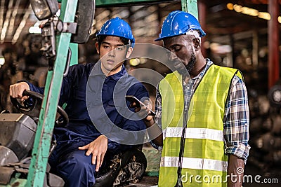 Engineer man wearing a safety helmet sitting on a forklift at the large warehouse where keep machine parts. Feeling bad at being Stock Photo