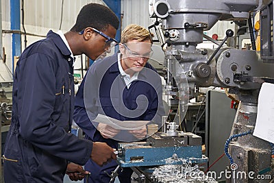 Engineer Showing Apprentice How to Use Drill In Factory Stock Photo