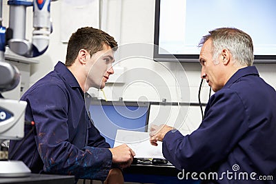 Engineer Showing Trainee Plans With CMM Arm In Foreground Stock Photo