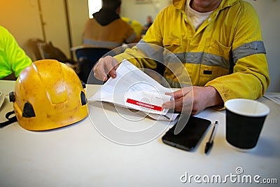 Engineer sitting placing safety hard hat on the table coffee cup pen reviewing JSA risk assessment Stock Photo