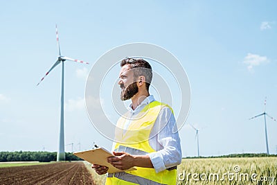 An engineer standing on a field on wind farm, making notes. Stock Photo