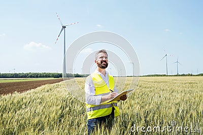 An engineer standing on a field on wind farm, making notes. Stock Photo