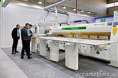 An engineer talks about the operation of woodworking equipment to a group of visitors at an exhibition Editorial Stock Photo