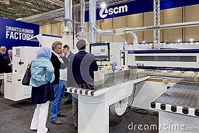 An engineer talks about the operation of woodworking equipment to a group of visitors at an exhibition Editorial Stock Photo