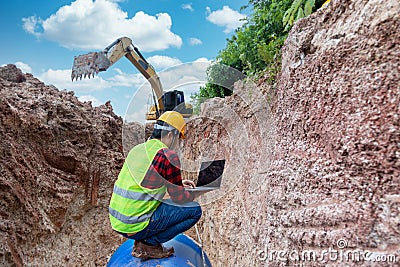 Engineer wear safety uniform use laptop examining excavation Drainage Pipe and Large plumbing water system underground at Stock Photo