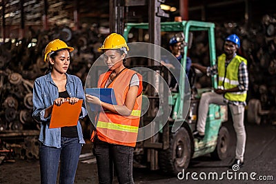 Engineer woman wearing helmet standing at the large warehouse where keep machine parts and holding clipboard. Used of vehicle part Stock Photo