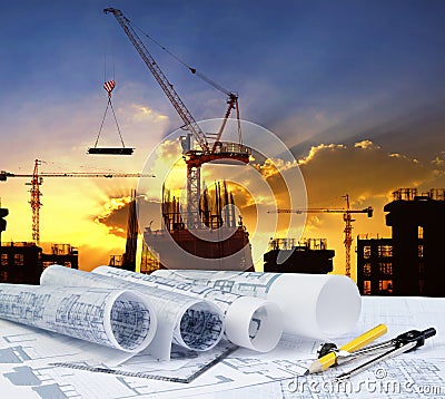 engineer working table plan, home model and writing tool equipment against building construction crane with evening dusky sky Stock Photo