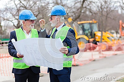 Engineers meeting and discussing blueprints while visiting work site Stock Photo