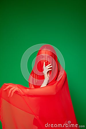 Mysterious woman covered with red veil against green background Stock Photo