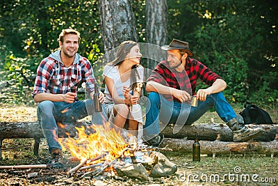 Enjoying camping holiday in countryside. Happy people sitting around campfire. Friends enjoy weekend barbecue in forest Stock Photo