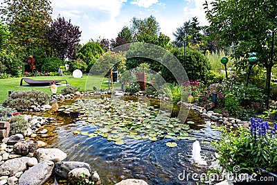 Garden with water lilies on pond, flowerbeds and trees in summer. Stock Photo