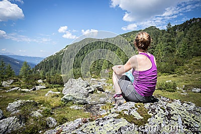 Enjoying the idyllic mountain landscape: Girl is sitting on a rock and resting Stock Photo