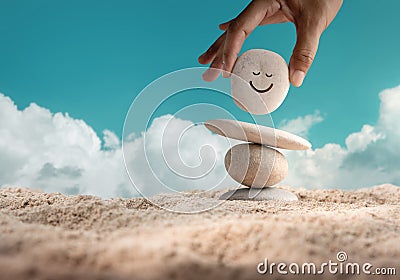 Enjoying Life Concept. Harmony and Positive Mind. Hand Setting Natural Pebble Stone with Smiling Face Cartoon to Balance on Beach Stock Photo