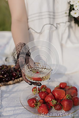 Enjoying taste. Unrecognizable woman in snow-white dress with glass of champagne with strawberries. Stock Photo