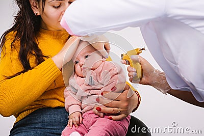 Enlarged photo. The doctor& x27;s hands are making holes in the ears with a pistol for a little baby. Stock Photo