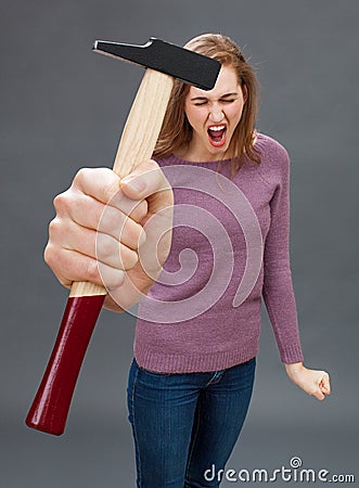 Enraged beautiful young woman shouting with hammer for DIY frustration Stock Photo