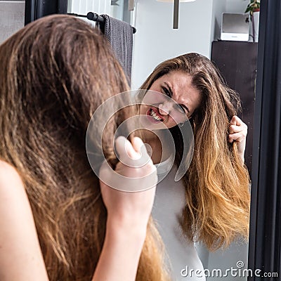 Enraged young woman pulling out her dry tousled long hair Stock Photo