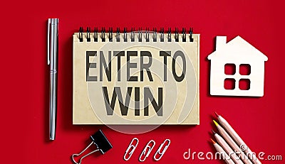 ENTER TO WIN text written on a notebook with pencils and office tools and model wooden house Stock Photo