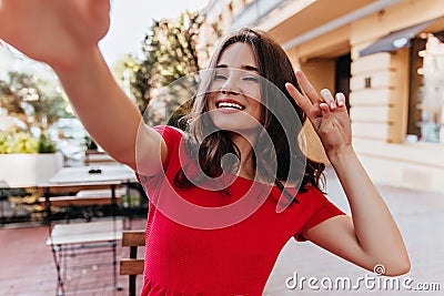 Enthusiastic caucasian lady making selfie in outdoor cafe. Laughing debonair woman taking picture of Stock Photo