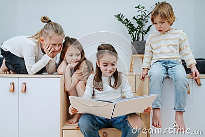 Enthusiastic girl reading a picture book to other children in a bedroom. Stock Photo