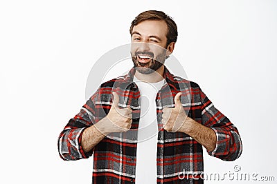 Enthusiastic male model winks and smiles, shows thumbs up, stands in checked shirt over white background Stock Photo