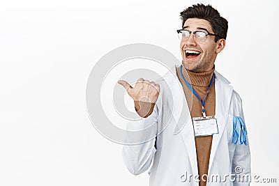 Enthusiastic male physician, happy doctor in glasses pointing and looking left, behind his shoulder, showing clinic Stock Photo