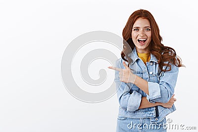 Enthusiastic sassy good-looking ginger girl with freckles in denim jacket pointing finger left, smiling amused and Stock Photo