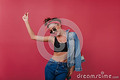 Enthusiastic sporty girl in sunglasses dancing on claret background. Studio shot of pleased black-haired woman in tank Stock Photo