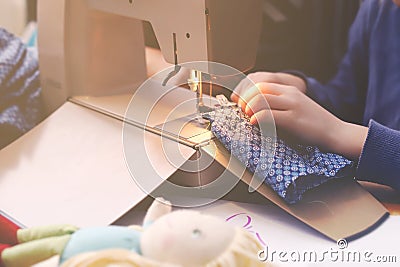 Enthusiastic young girl sews a toy dress for her doll at a compact sewing machine under supervision of her mother Stock Photo