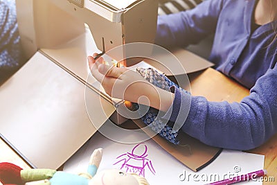 An enthusiastic young girl works with a compact sewing machine under supervision of her mother to make a toy dress for her doll Stock Photo